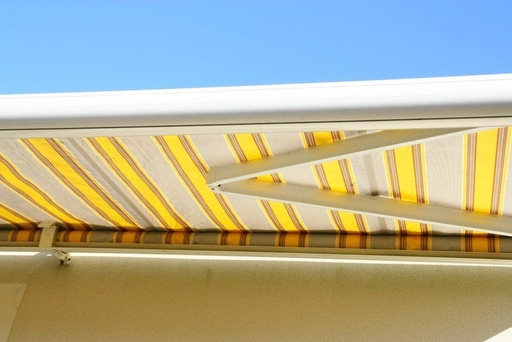 Una tenda a strisce gialle e bianche si estendeva da un edificio bianco contro un cielo blu.