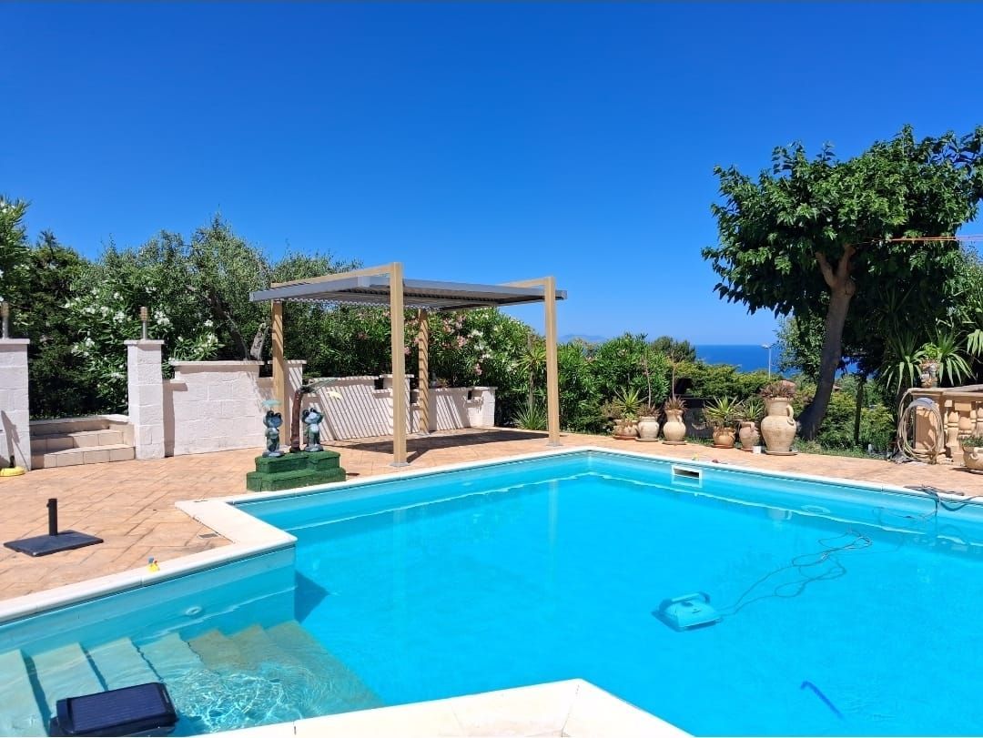 Piscina con pergolato, con vista sull'oceano sotto un cielo azzurro e limpido.
