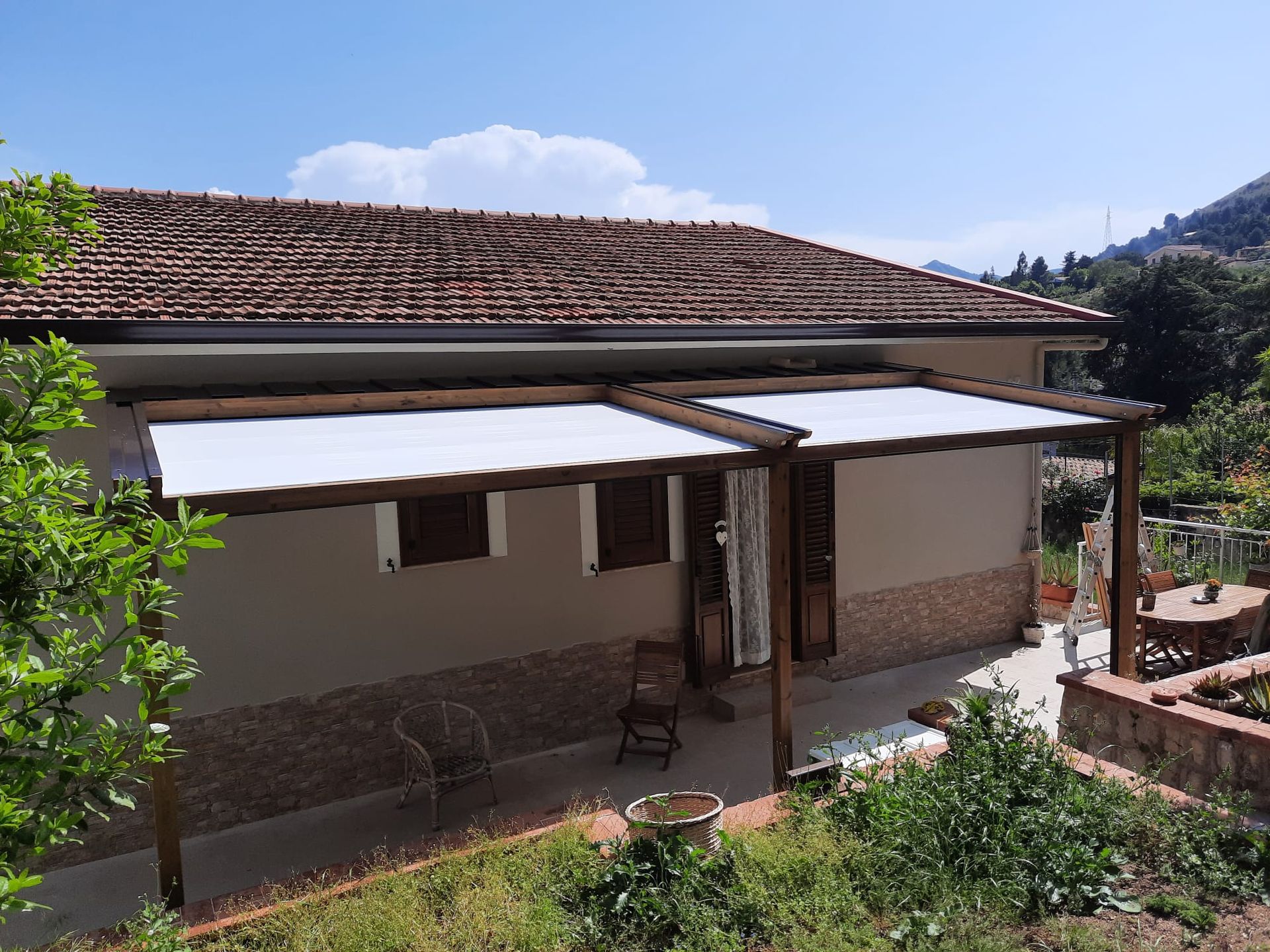 Casa color marrone chiaro con tetto di tegole marroni; tende da sole bianche retrattili coprono un patio.