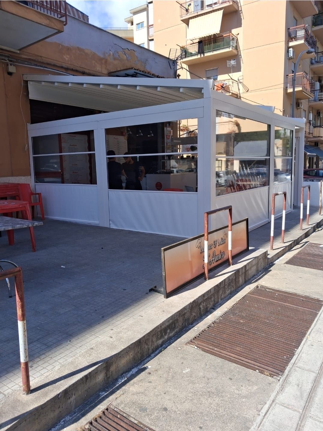 Area salotto all'aperto con tenda bianca, pareti in tela e cartelli sul marciapiede.