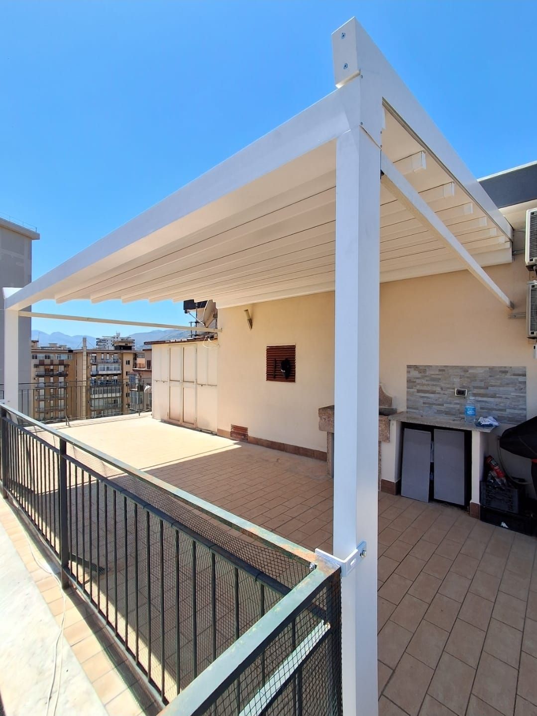 Un pergolato bianco ricopre una terrazza panoramica con ringhiera e vista sulla città nelle giornate di sole.