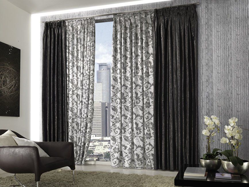 Finestra con tende a motivi grigi e neri e vista sulla città. In primo piano una poltrona marrone.