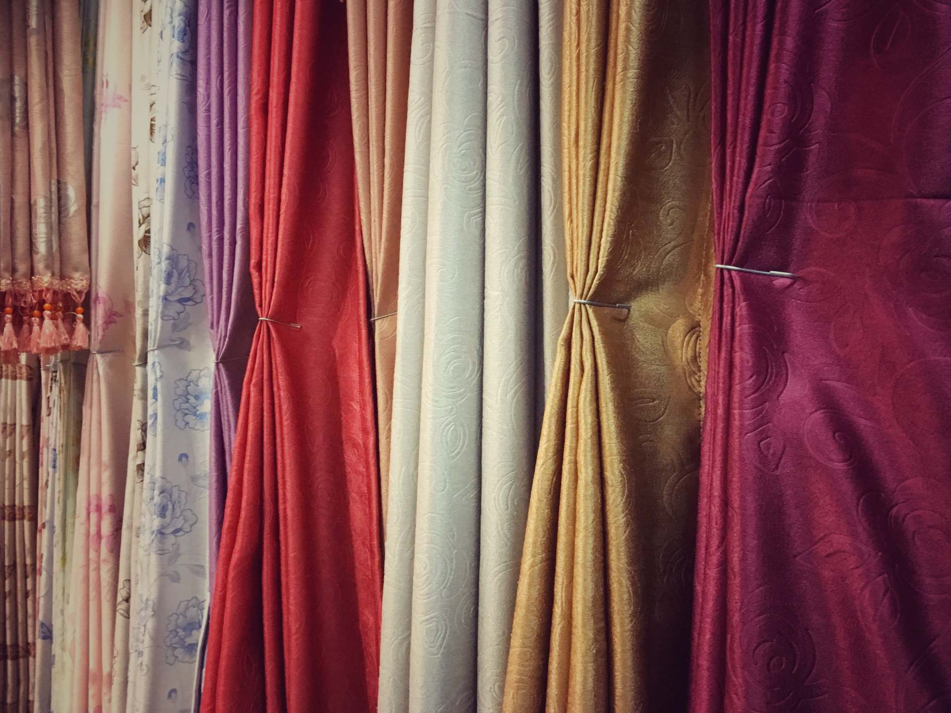 Tende di vari colori appese una accanto all'altra: rosso, oro, viola, bianco e altri.