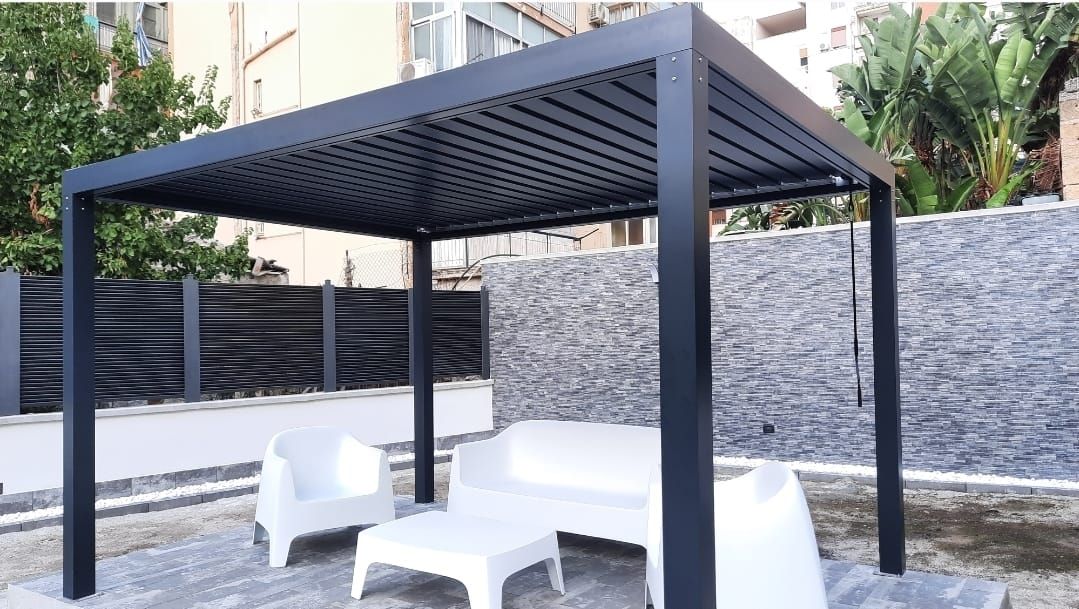 Pergola nera con tetto regolabile sopra mobili da esterno bianchi in un patio.