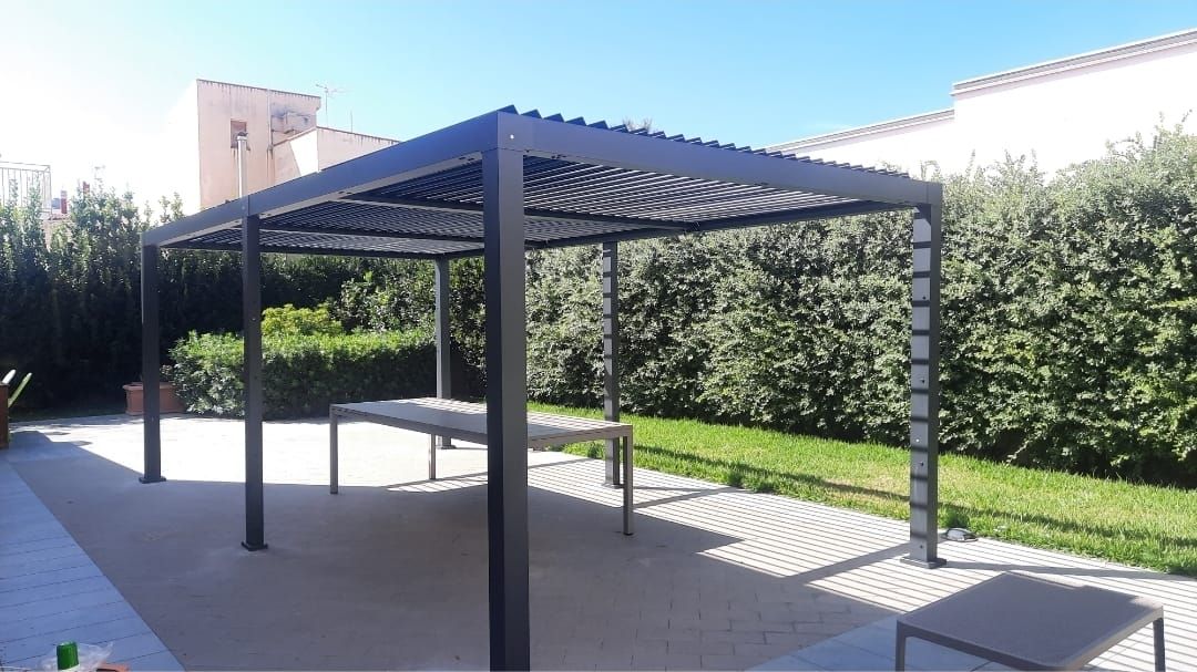 Pergola con tetto a doghe regolabili sopra il patio, tavoli a vista all'interno, ambiente esterno soleggiato.