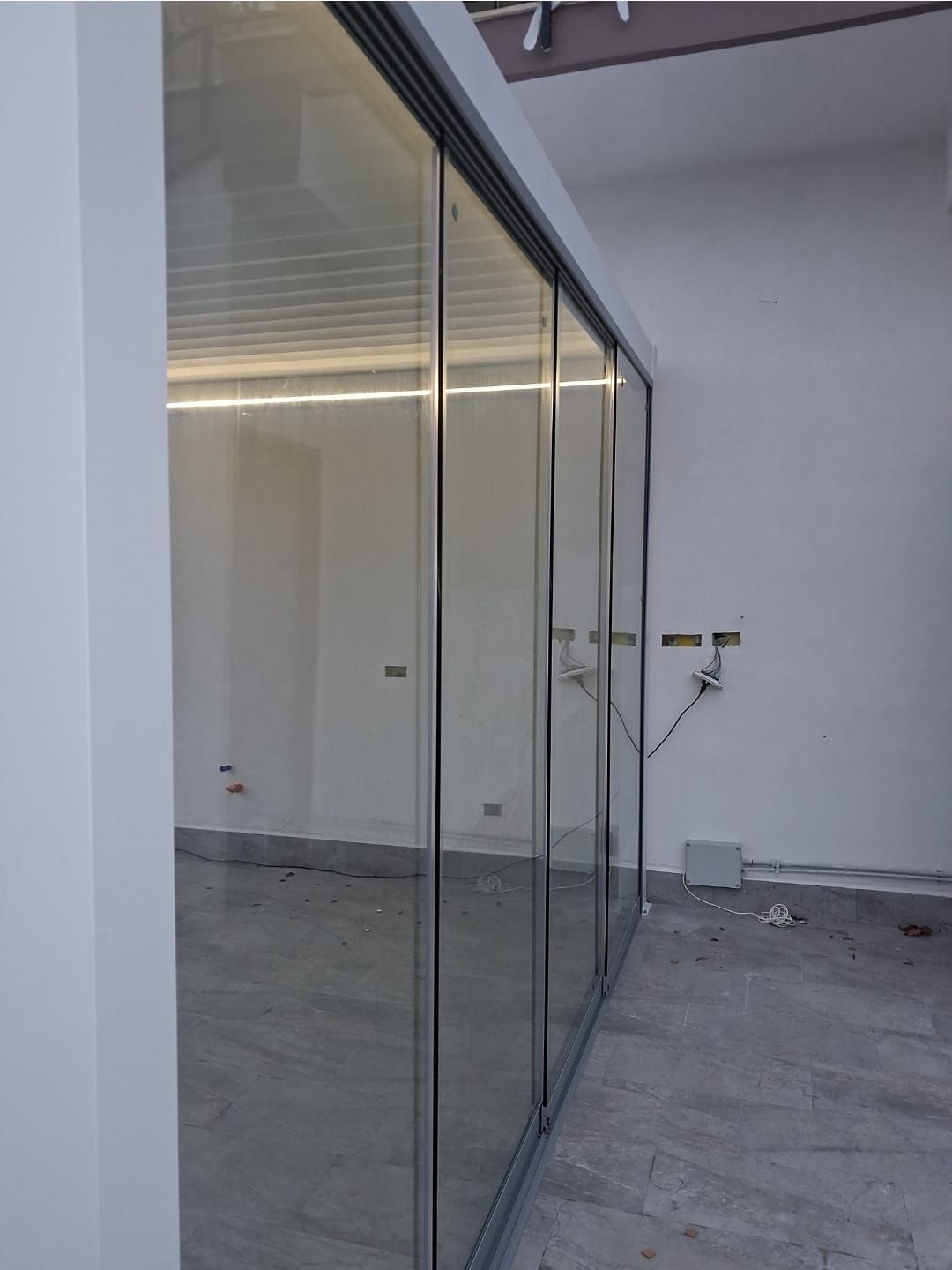 Porte scorrevoli in vetro in una stanza grezza con pareti bianche e pavimento in cemento.