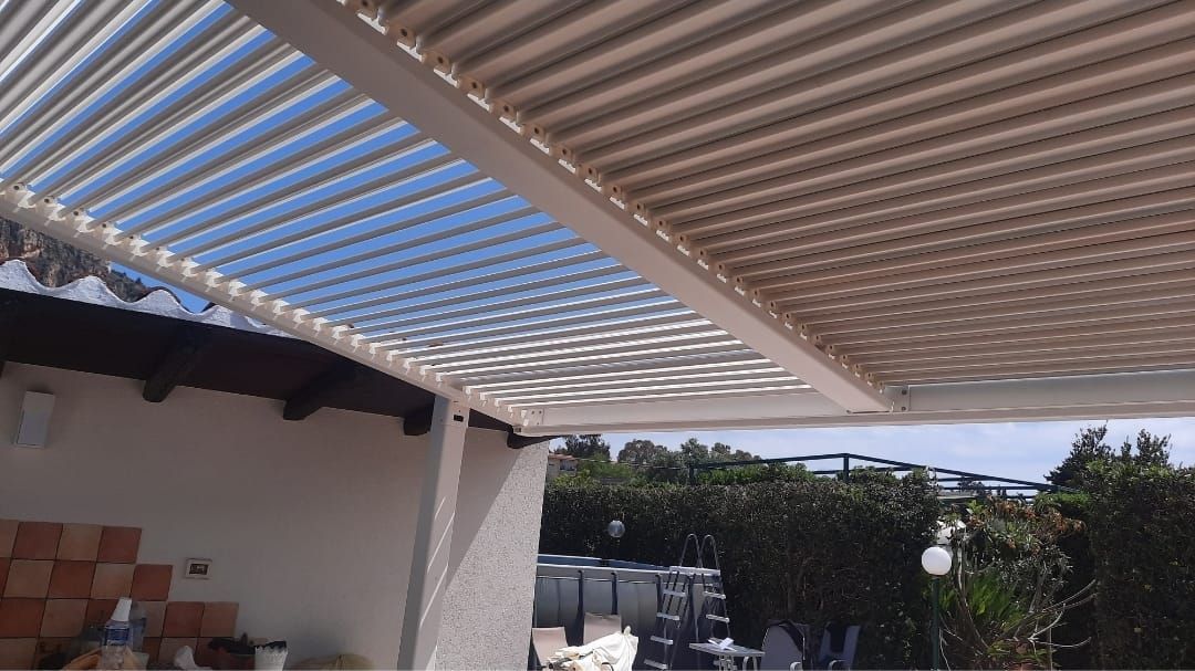 Tetto a pergola con lamelle regolabili; cielo azzurro visibile.