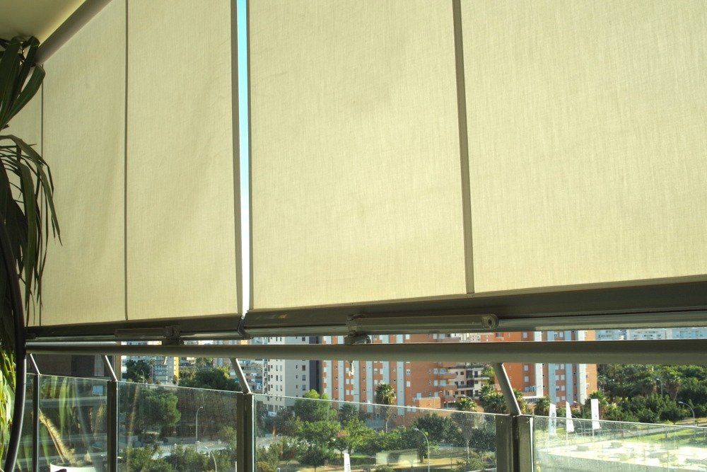 Tende a rullo beige che coprono parzialmente una finestra con un paesaggio urbano visibile sullo sfondo.
