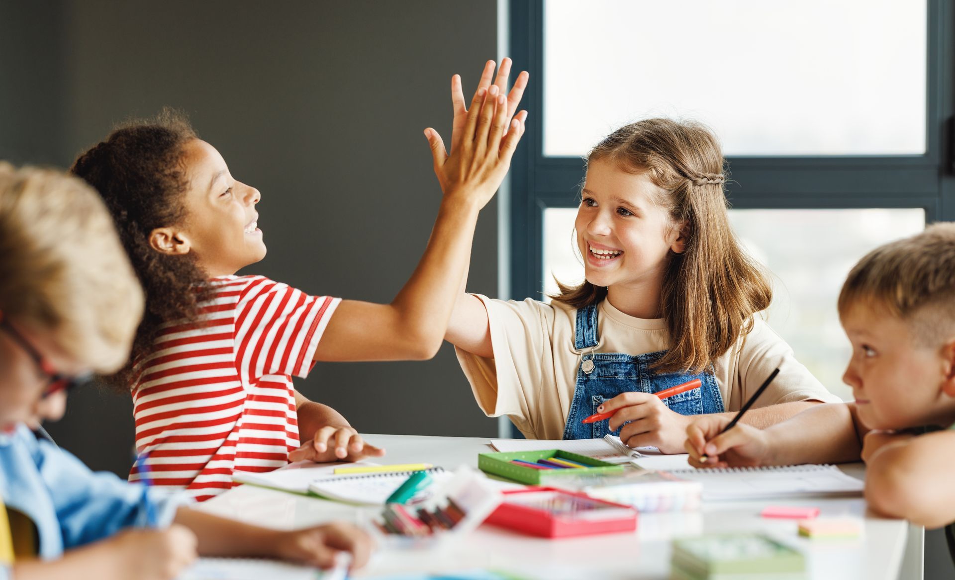 Children sitting at table high-fiving 