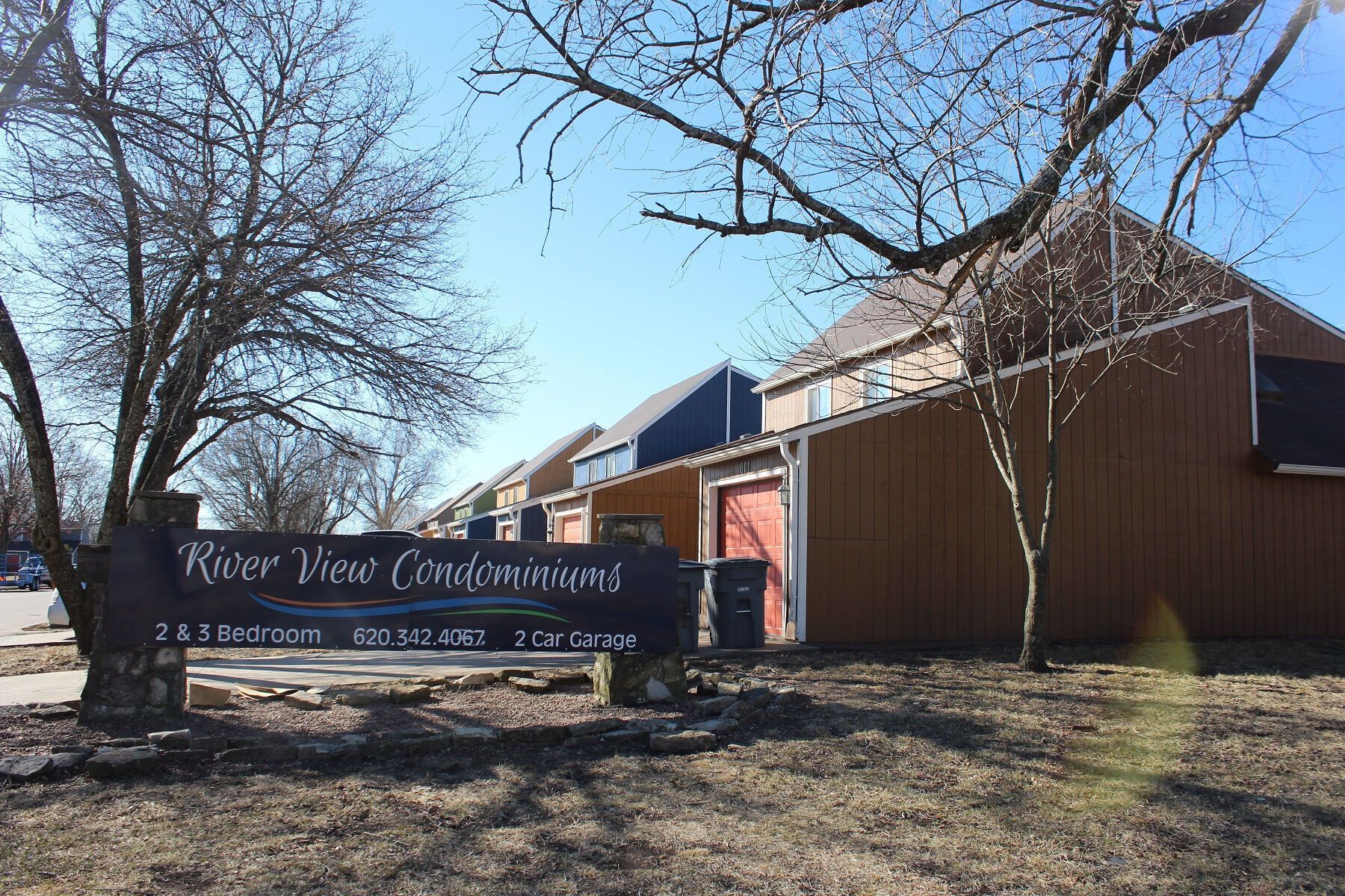 River View Condominiums sign in front of brown and blue buildings on a sunny day.