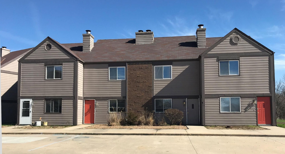 Brown and gray townhouses with red and white doors under a clear blue sky.