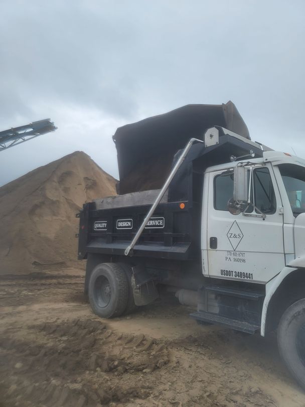 Z&S Construction LLC dump truck getting loaded with topsoil in Hazleton PA with large soil piles under cloudy skies.