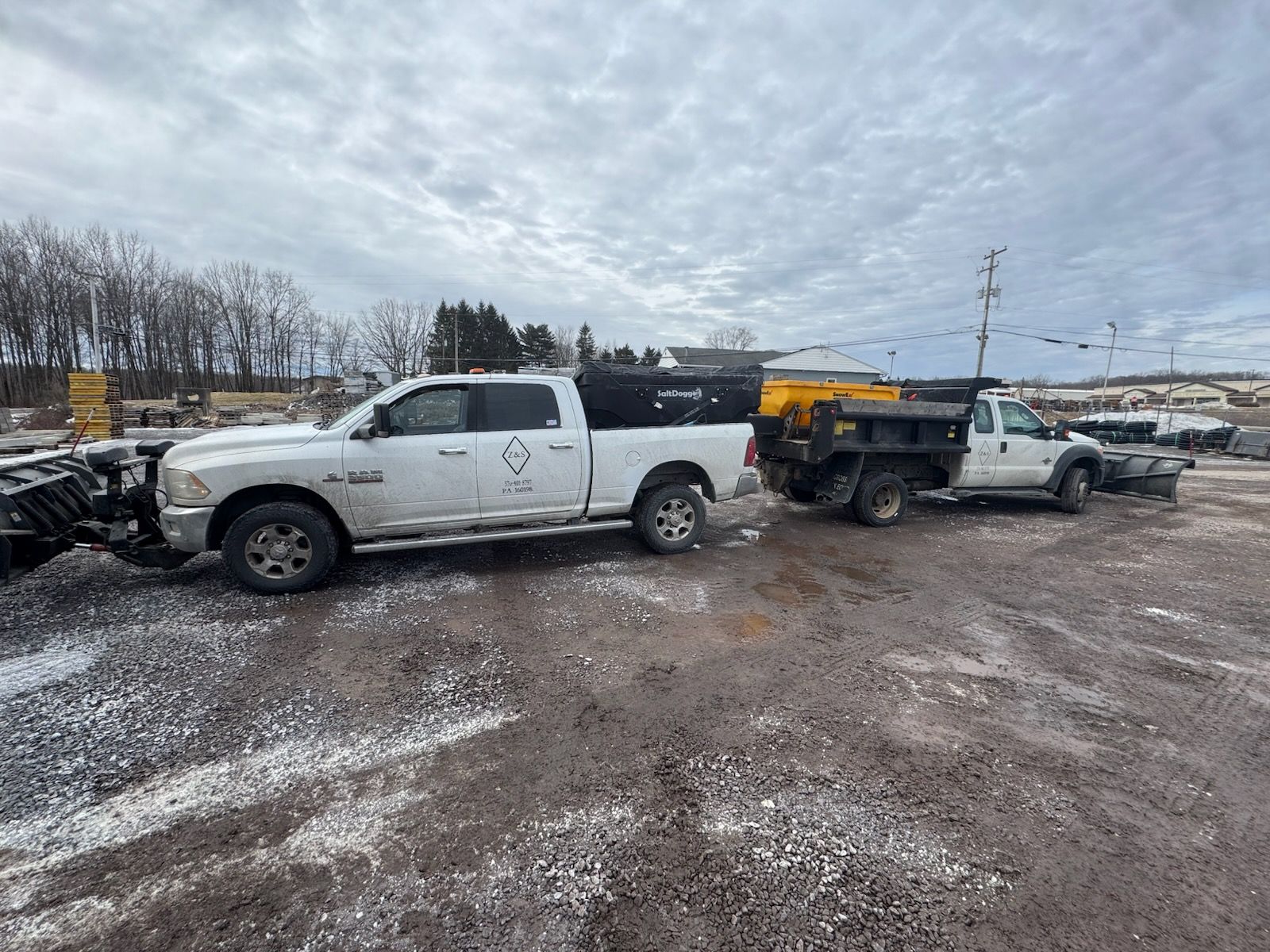 Z&S Construction clearing snow in Hazleton, PA with a skid steer snow pusher. Z&S Construction LLC trucks equipped with snow plows and salt spreaders parked on a gravel lot in Hazleton, Pennsylvania.