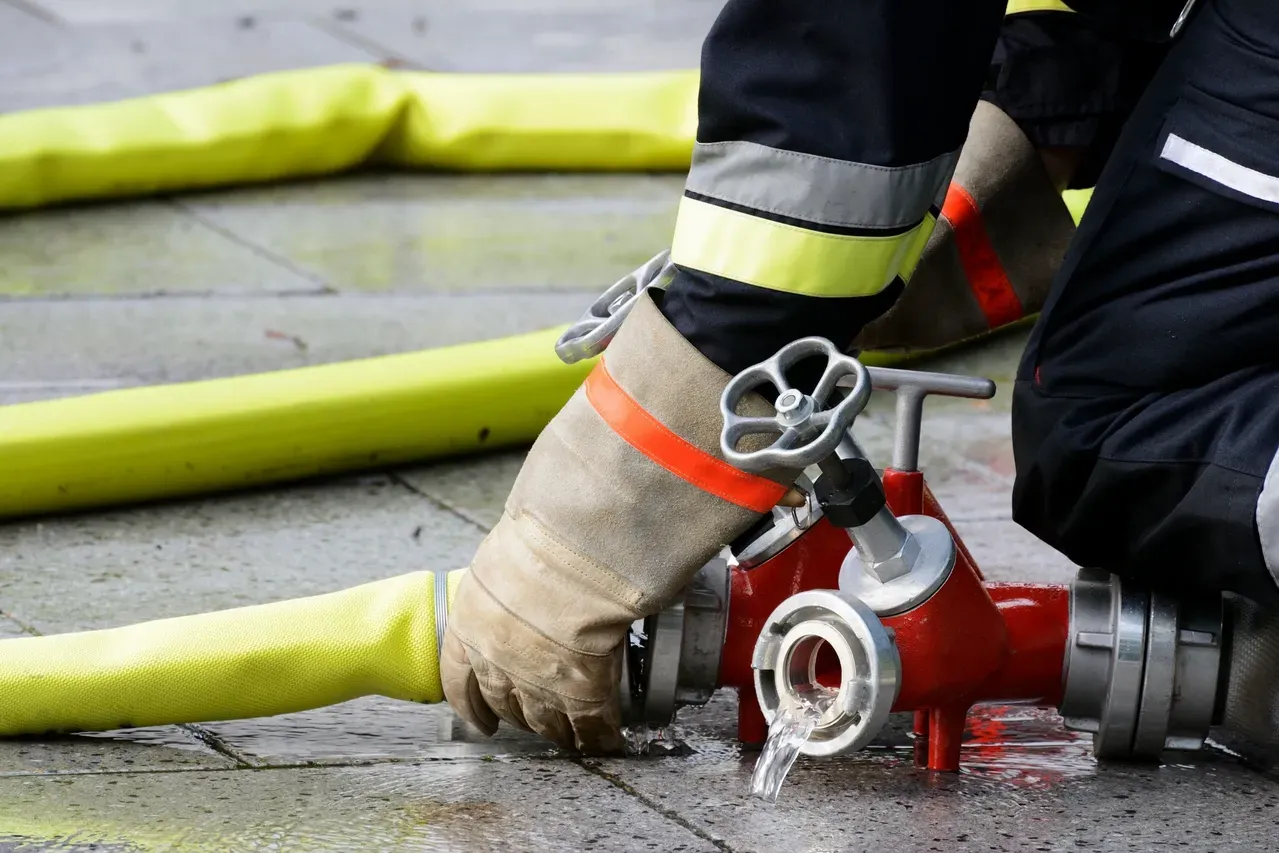 A fireman is connecting a fire hose to a fire hydrant.