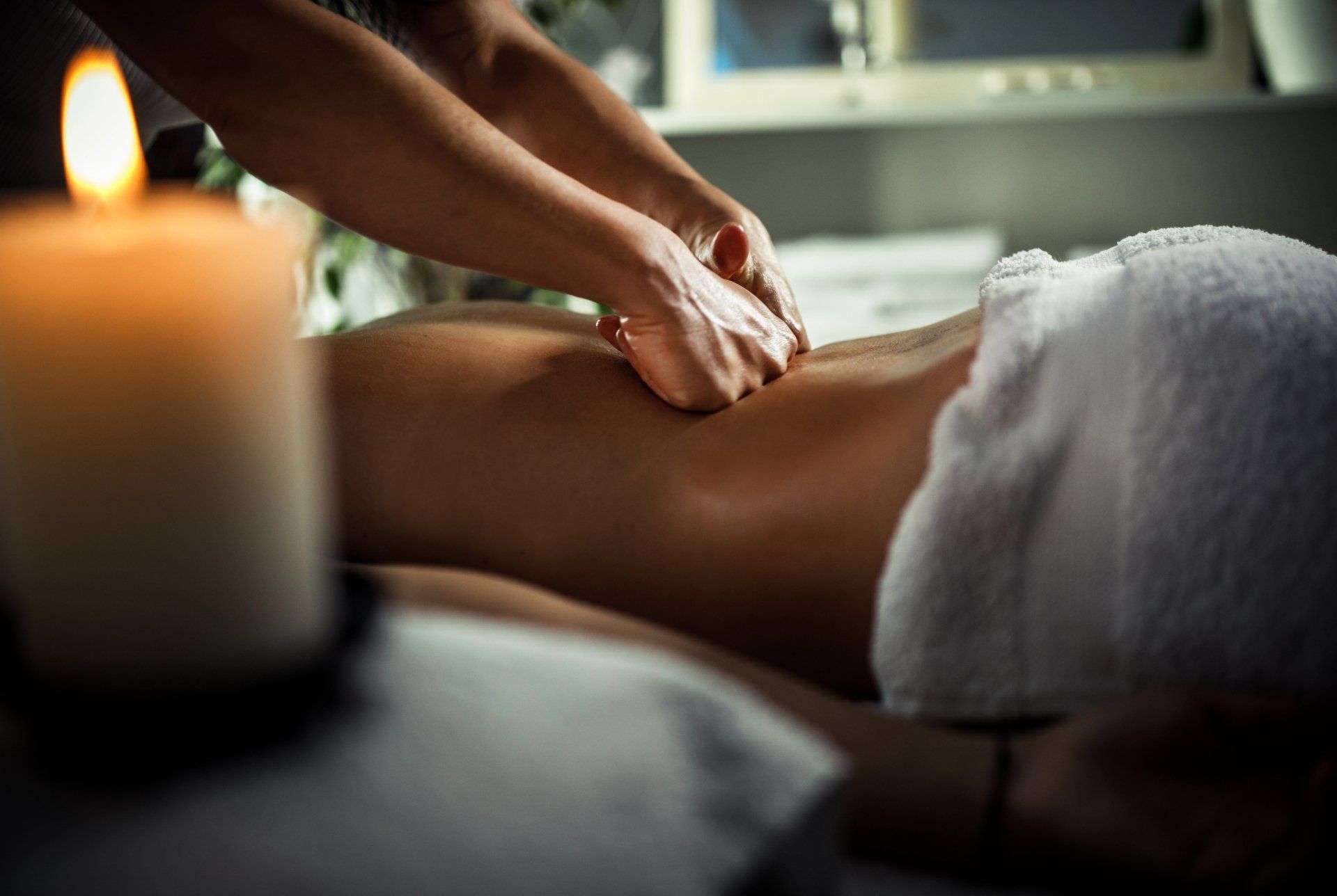 Una donna si sta facendo fare un massaggio in una spa con una candela sullo sfondo.