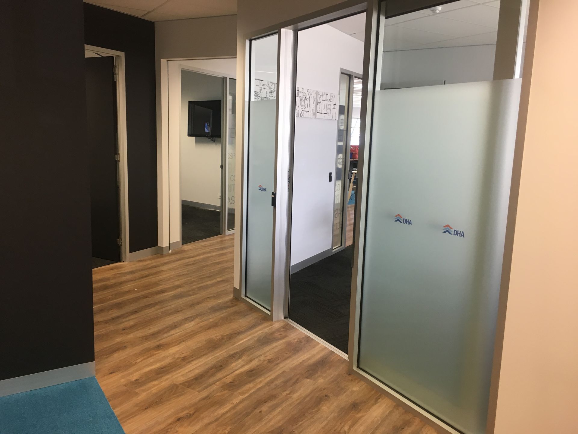 Office hallway with wood flooring, glass doors with frosted accents, and multiple doorways — AKW Builders Pty Ltd In Leanyer, NT