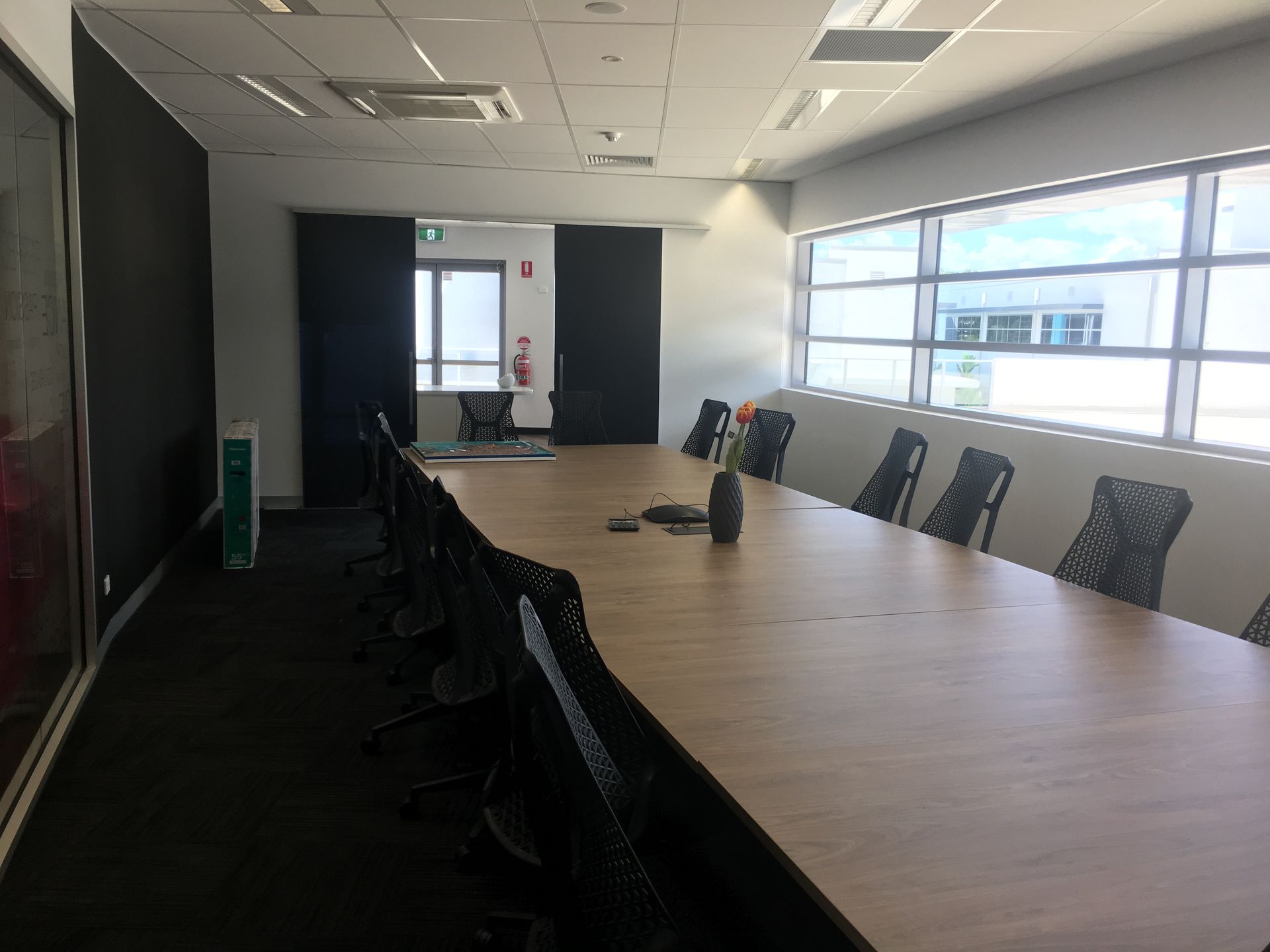 Long conference table with chairs in a modern office, windows on the right, dark walls, and a view of the outside — AKW Builders Pty Ltd In Leanyer, NT