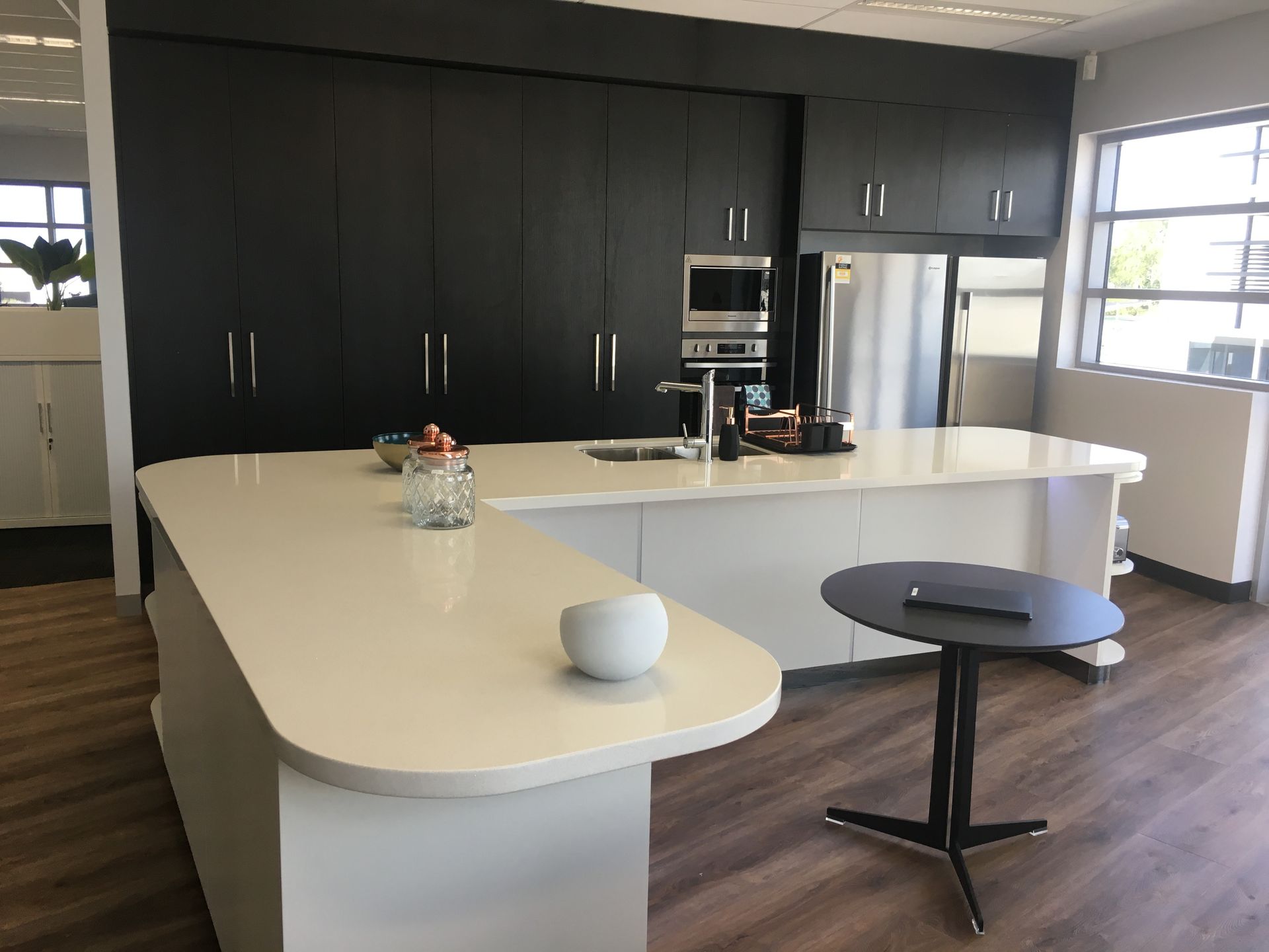 Modern office kitchen with black cabinets, white island, and small round table — AKW Builders Pty Ltd In Leanyer, NT