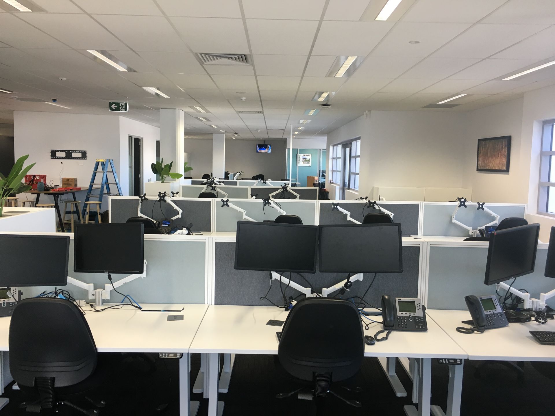 Office with multiple cubicles, each with a desk, two monitors, phone, and chair. Bright overhead lighting — AKW Builders Pty Ltd In Leanyer, NT