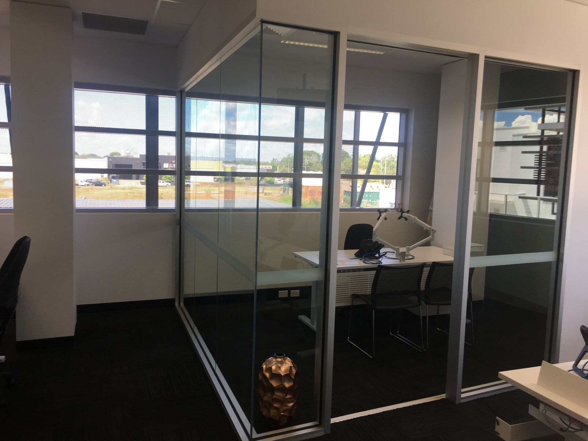 Glass-walled office cubicle with a desk and chairs, set against windows with an outside view — AKW Builders Pty Ltd In Leanyer, NT