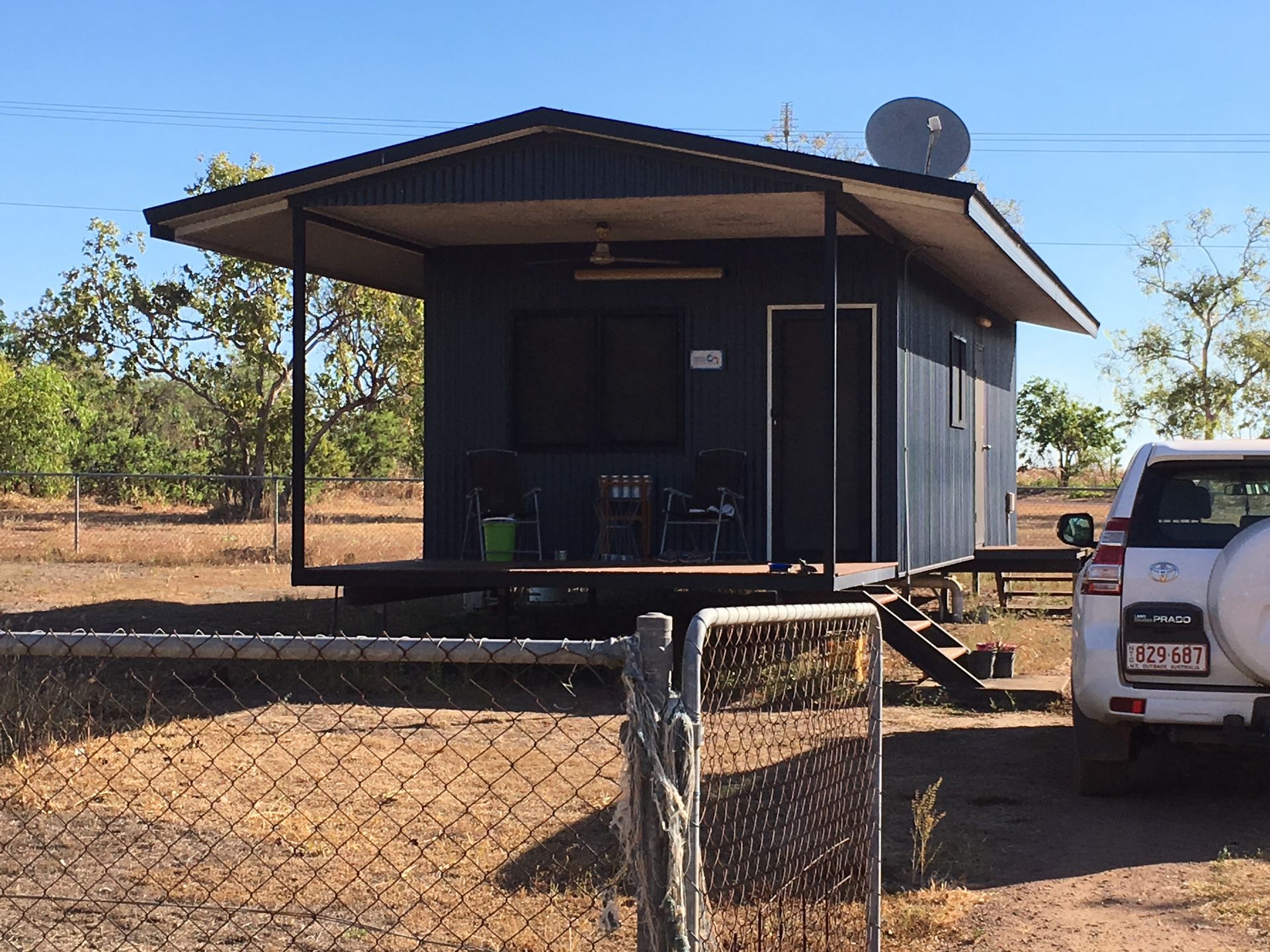 Small blue cabin with covered porch, satellite dish, and white SUV in a rural setting — AKW Builders Pty Ltd In Leanyer, NT