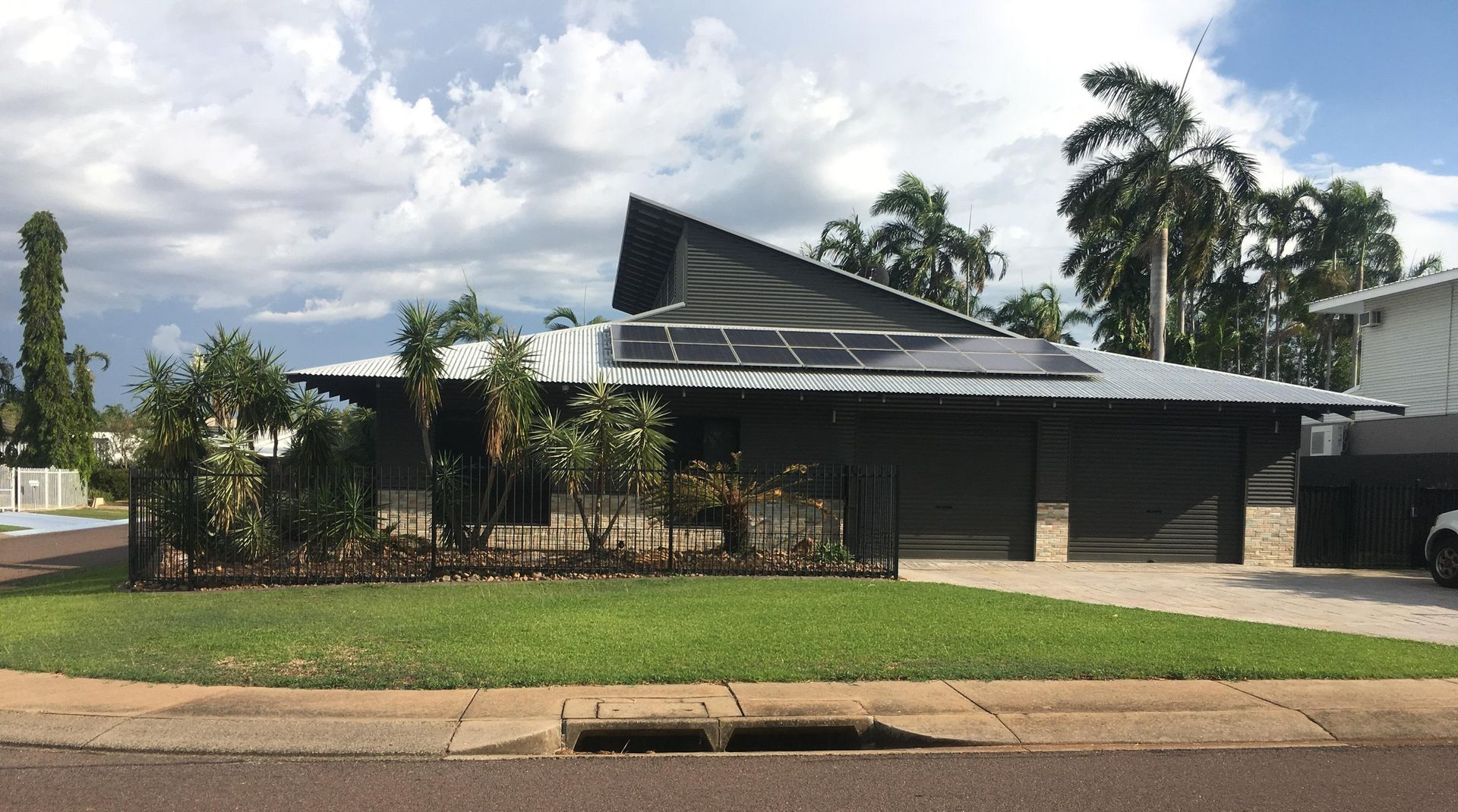 Modern house with dark grey exterior, solar panels on roof, and manicured lawn — AKW Builders Pty Ltd In Leanyer, NT