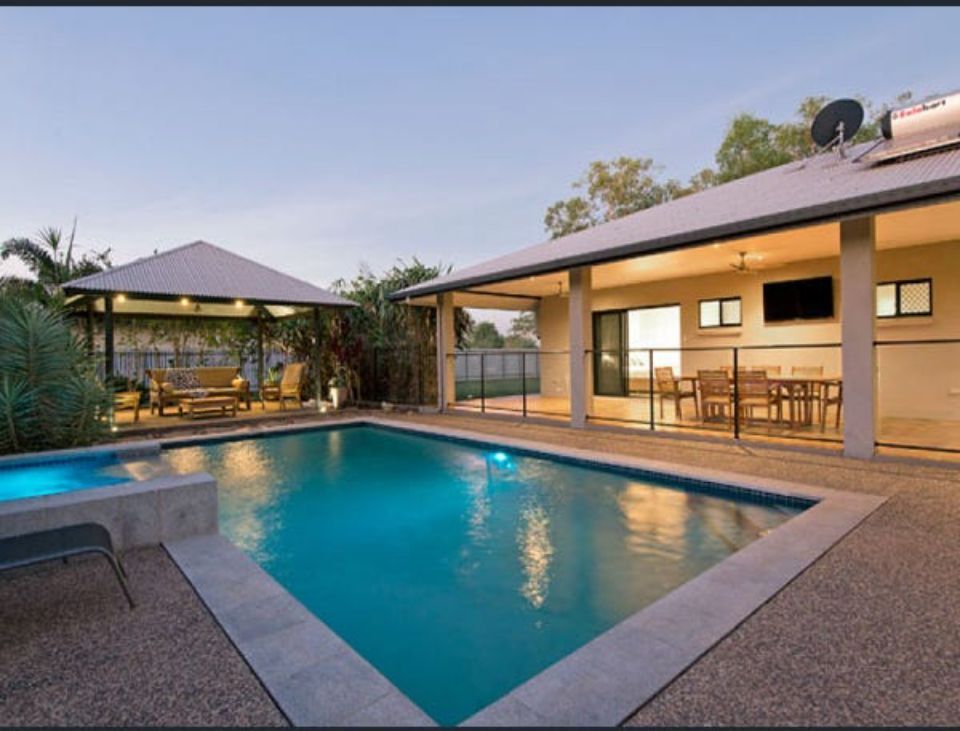 Backyard with pool, patio, gazebo, and house at dusk. Blue pool, beige patio, neutral-coloured structures — AKW Builders Pty Ltd In Leanyer, NT