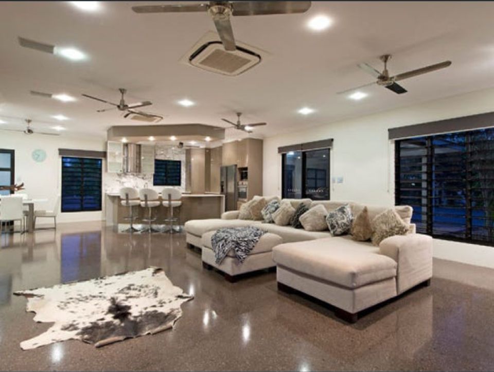 Spacious living room with beige sectional, cowhide rug, and open kitchen with bar seating; grey floors and white walls — AKW Builders Pty Ltd In Leanyer, NT