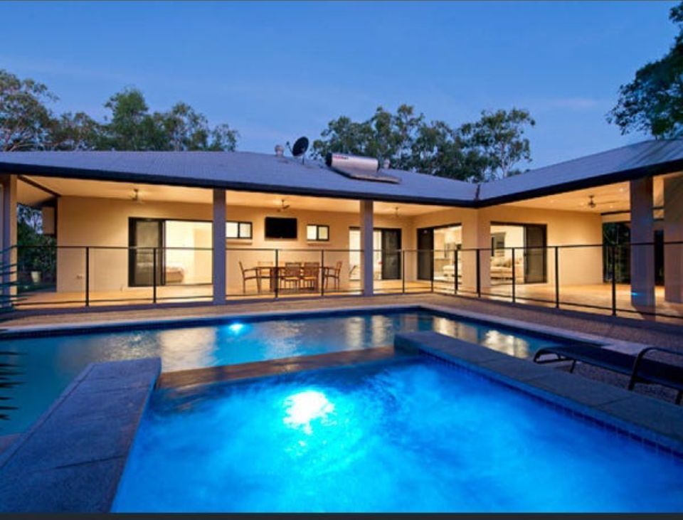 A home with a blue swimming pool in front. The house has large glass doors and an outdoor dining area — AKW Builders Pty Ltd In Leanyer, NT