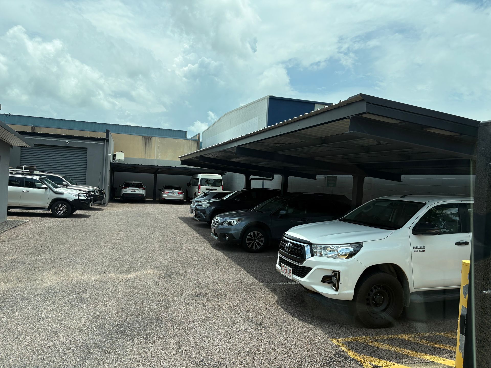 Parking lot with several cars parked under a covered structure, grey gravel surface, cloudy sky — AKW Builders Pty Ltd In Leanyer, NT