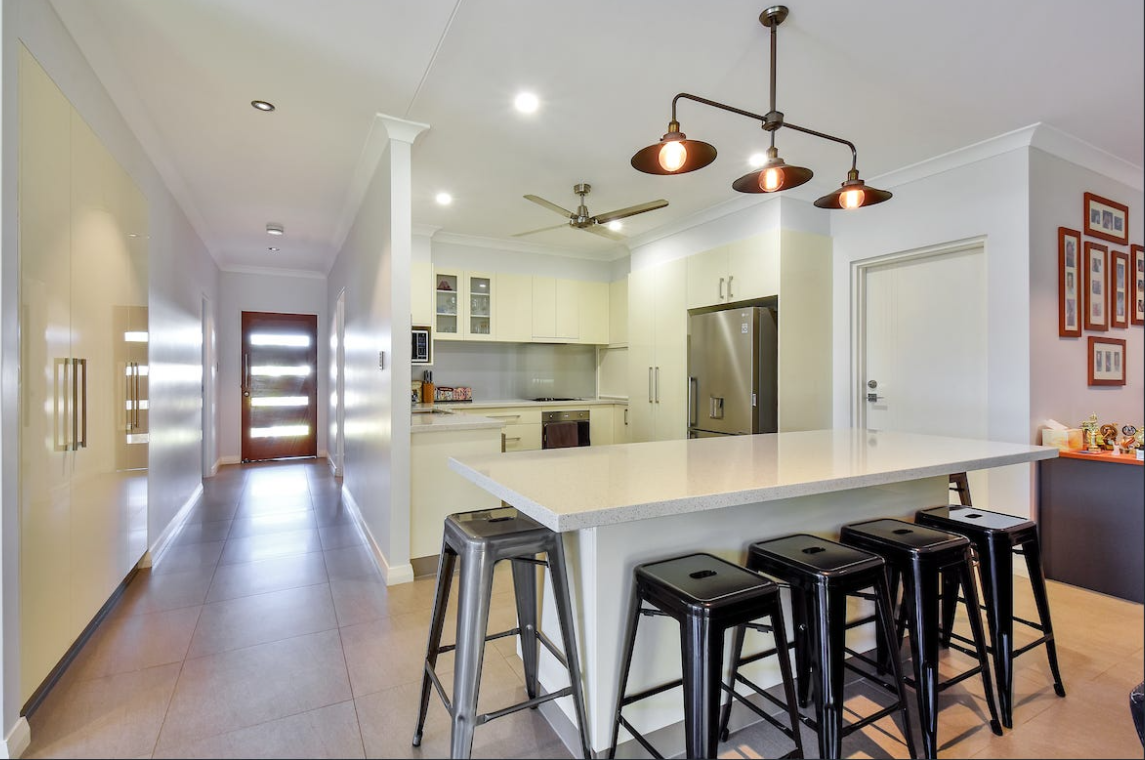 Interior view of a kitchen with an island, stools, and a hallway leading to a door — AKW Builders Pty Ltd In Leanyer, NT