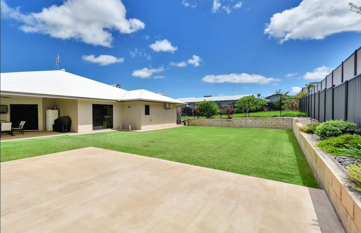Backyard with green lawn, concrete patio, beige house, and blue sky with clouds — AKW Builders Pty Ltd In Leanyer, NT