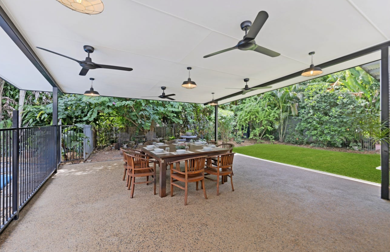 Outdoor dining area with a long wooden table, chairs, and ceiling fans. Lush greenery surrounds the patio — AKW Builders Pty Ltd In Leanyer, NT
