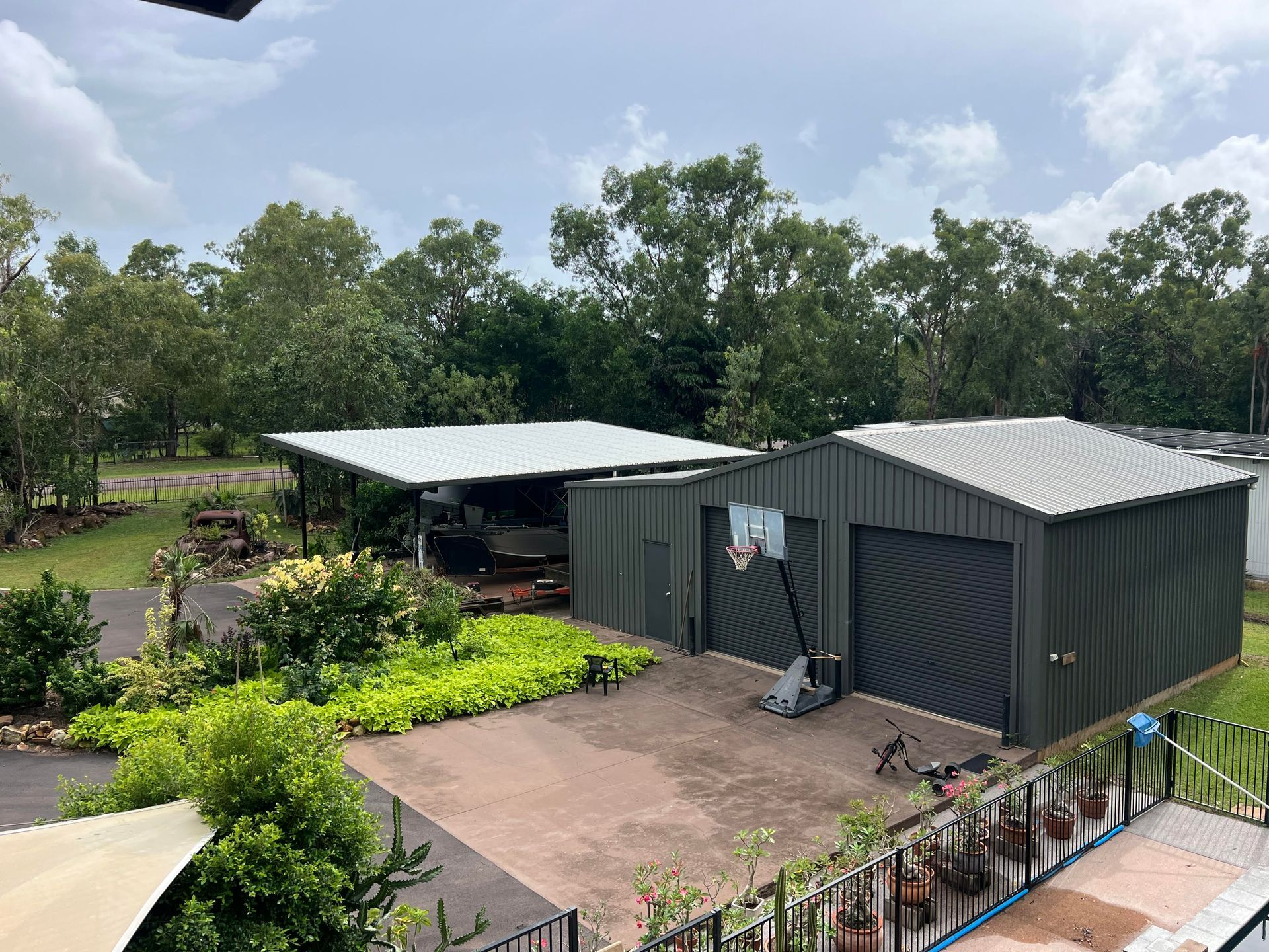 Green metal sheds and carport in a yard, trees in background, overcast sky — AKW Builders Pty Ltd In Leanyer, NT