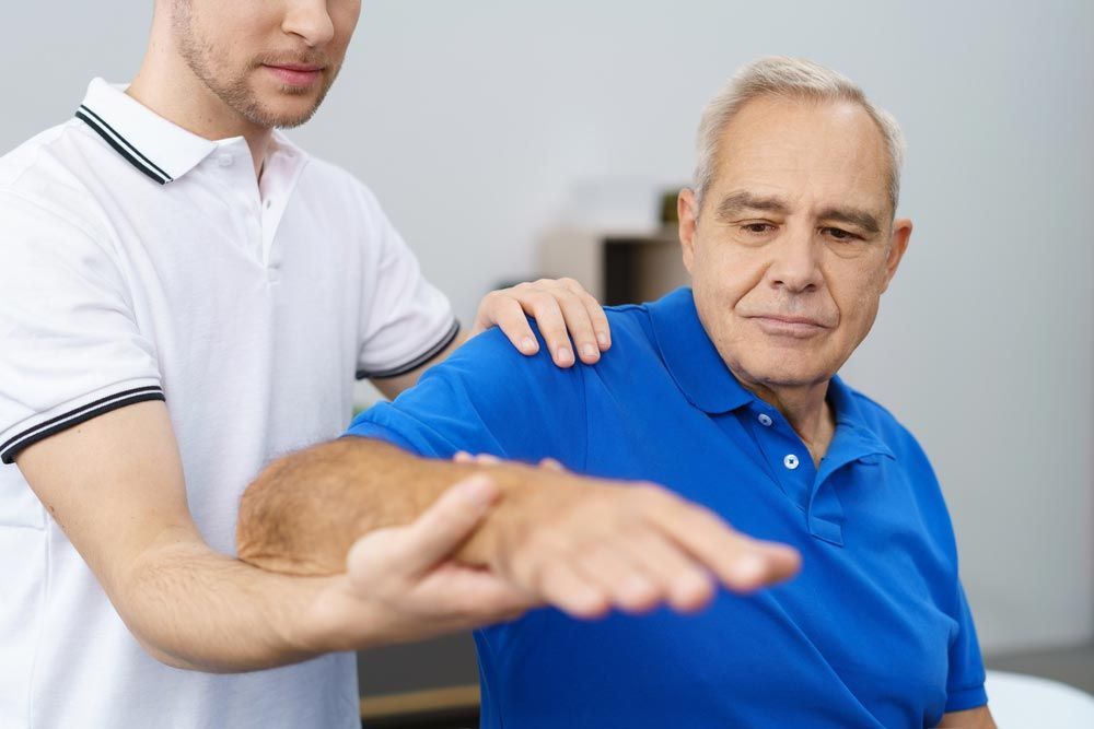 Guy Helping An Old Man Doing Arm Stretching
