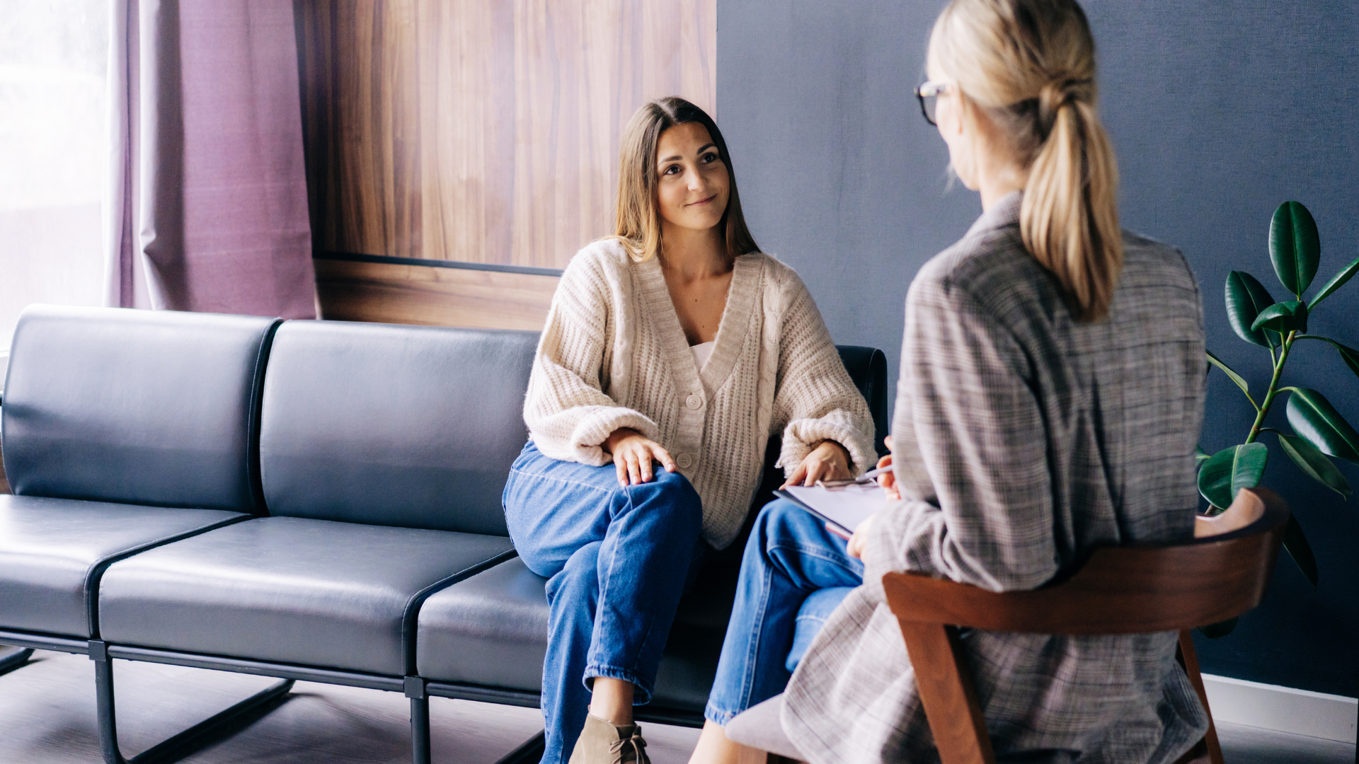 Two women are sitting on a couch talking to each other.