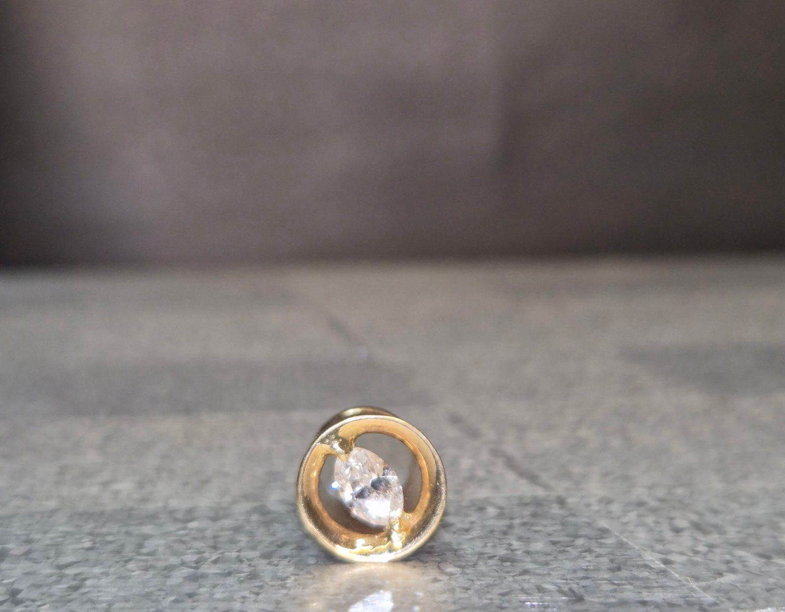 Gold earring with a diamond set in a round frame, resting on a gray surface.
