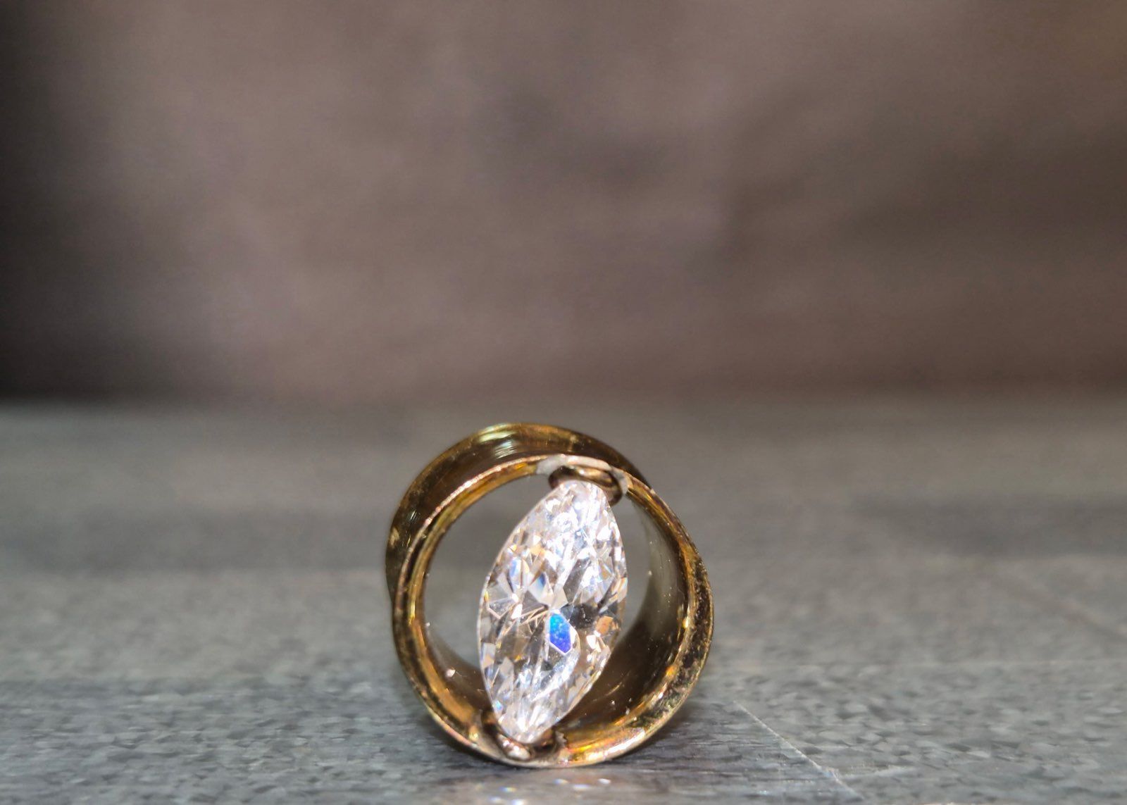 A gold ring with a marquise-cut diamond on a dark grey surface.