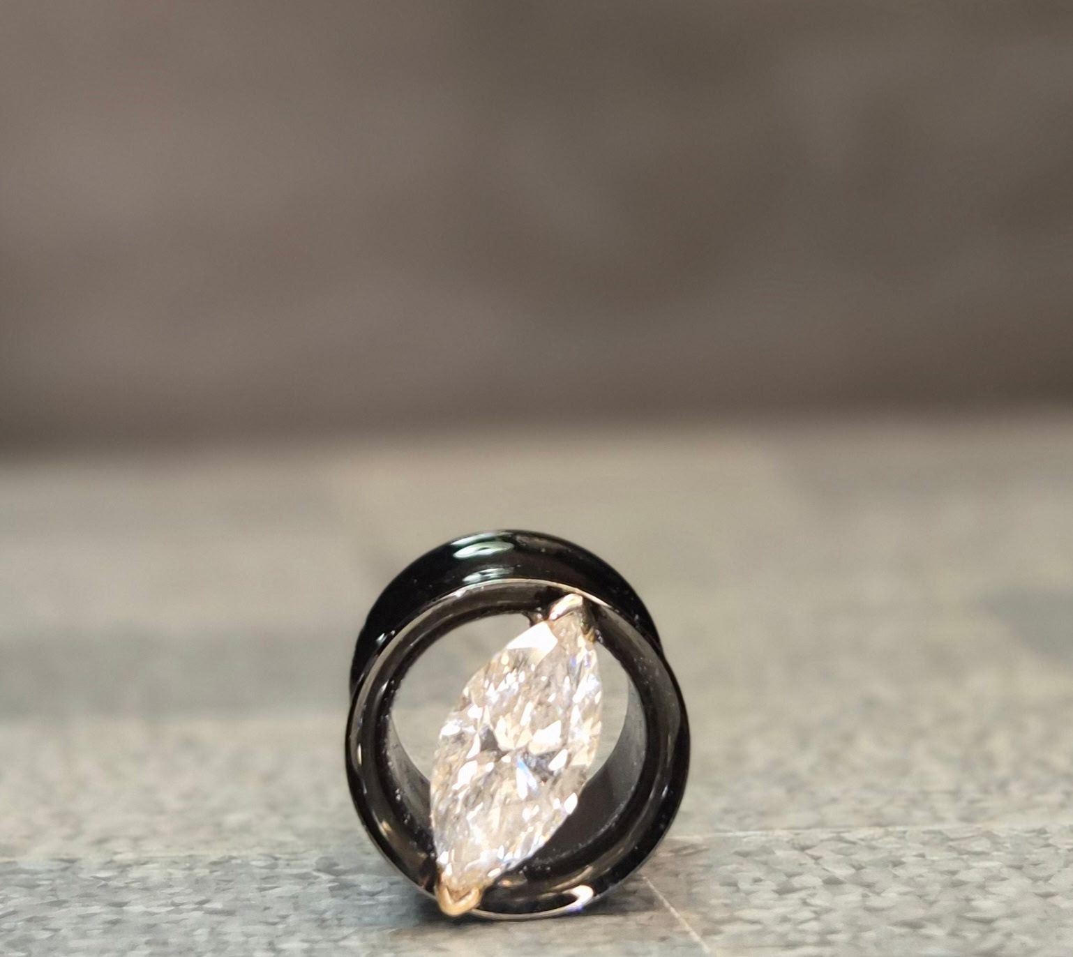 Black ear gauge with a clear, marquise-shaped gem in the center, on a gray surface.