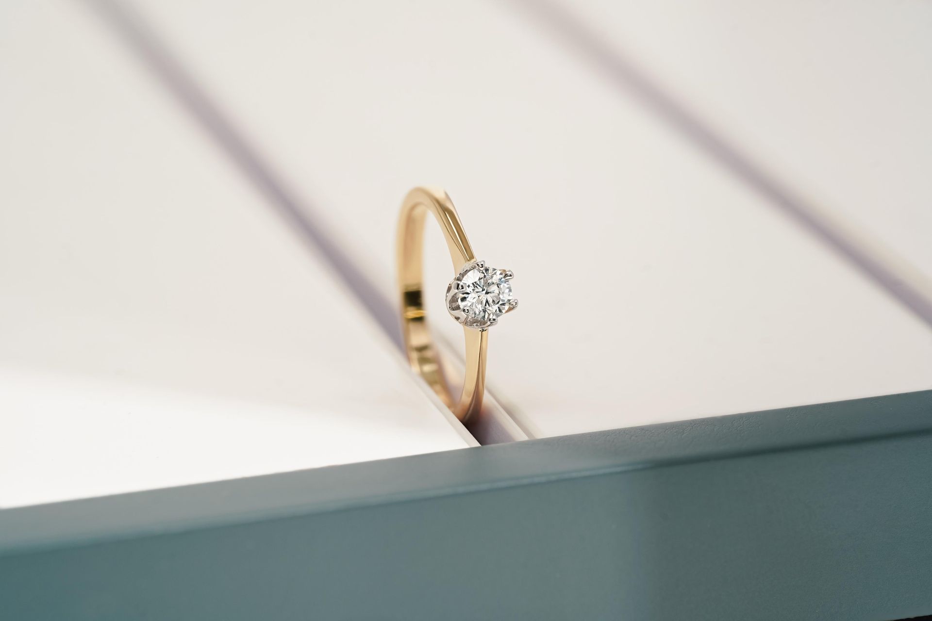 Gold ring with a diamond set in a white display case.