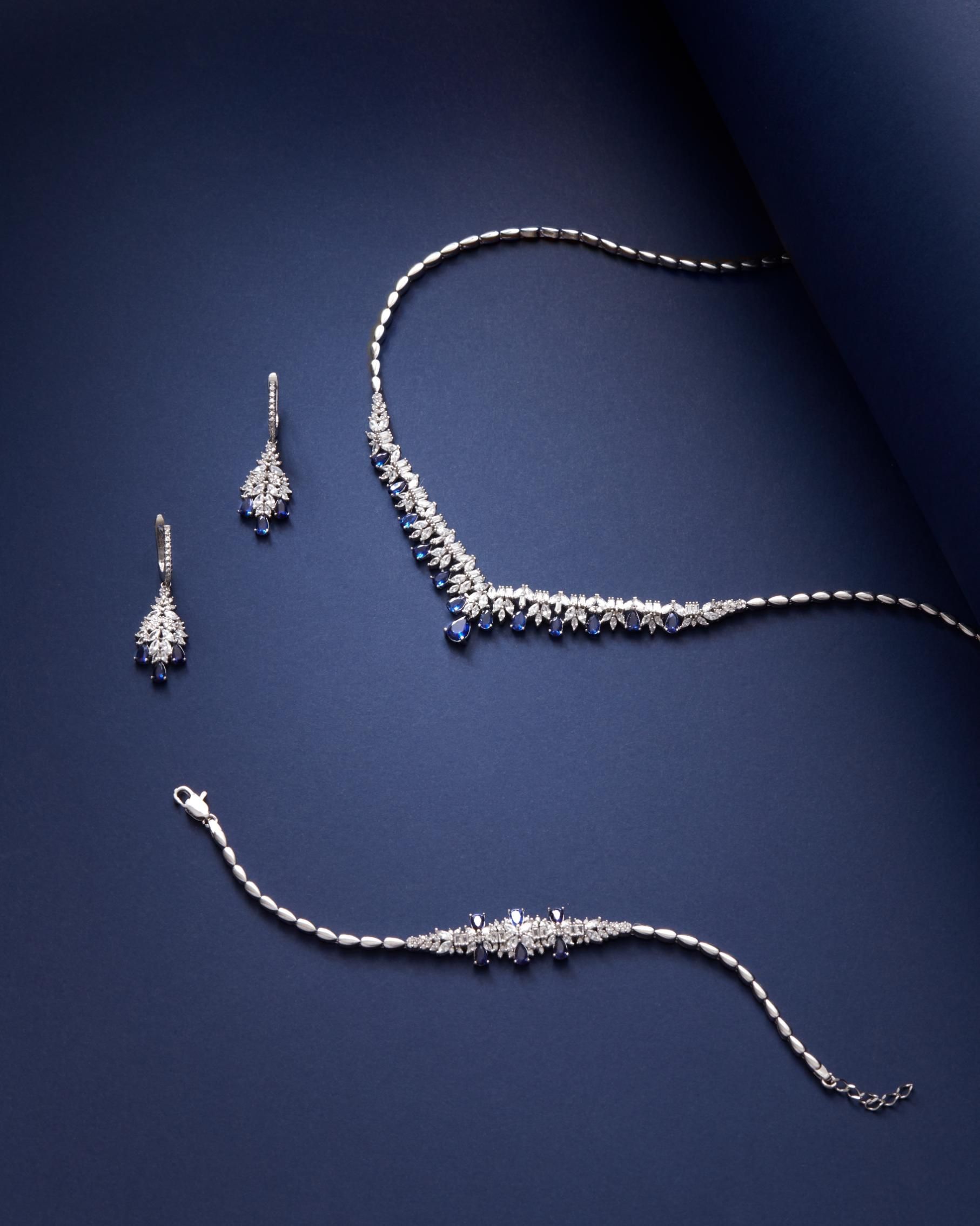 Diamond jewelry set on a dark blue background: necklace, earrings, and bracelet.