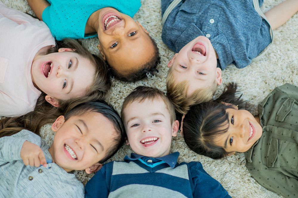 Children lying in a circle, smiling and laughing on a light carpet.