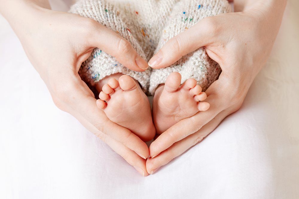Hands forming a heart around a baby's tiny feet.