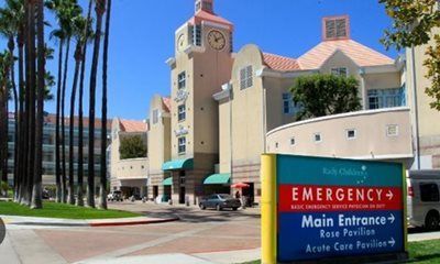 Hospital exterior with a clock tower and a sign pointing to the emergency and main entrances.