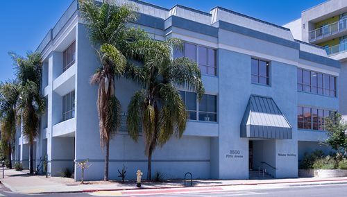 Blue office building with palm trees in front; sidewalk and street visible.