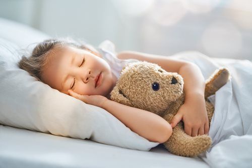 Child sleeping, hugging a teddy bear in bed.