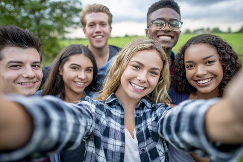 Group of smiling young people taking a selfie outdoors, wearing casual clothing.