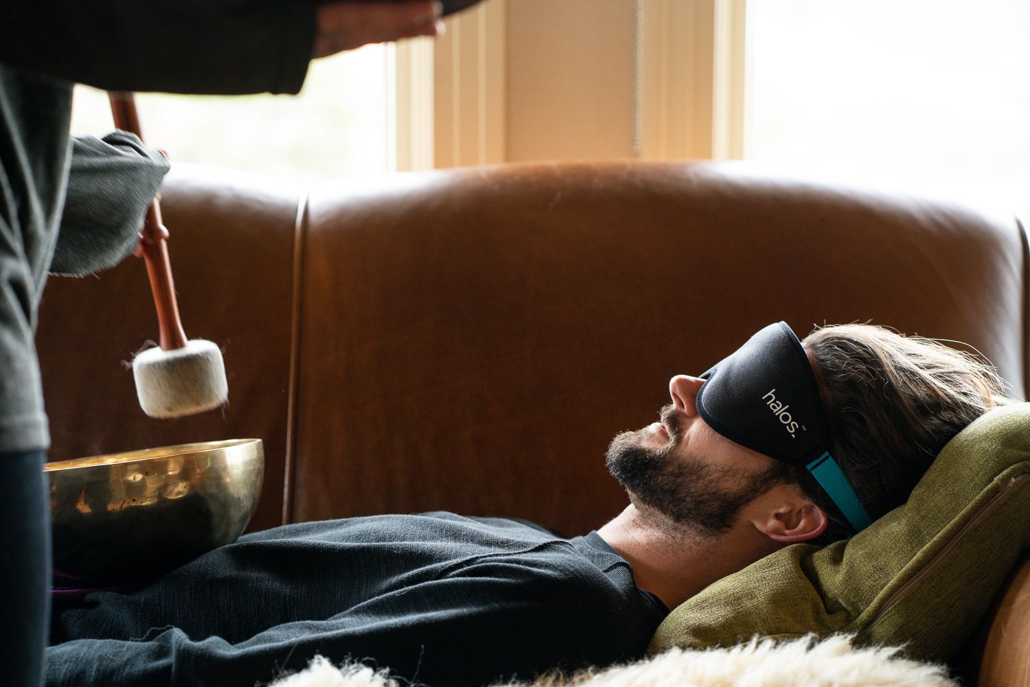 Man with eye mask receiving sound bath treatment, indoors.