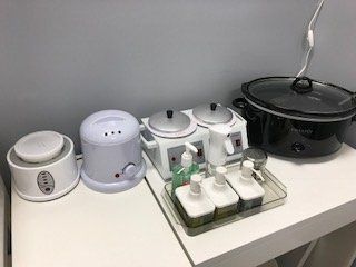 A table with a crock pot , wax warmers , and soap dispensers on it.