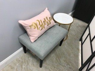 A pink pillow is sitting on a gray ottoman next to a small table.